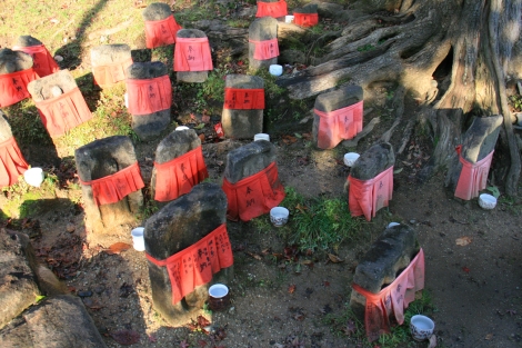8. Statuettes vétues de rouge avec un petit verre de saké posé devant chacune.